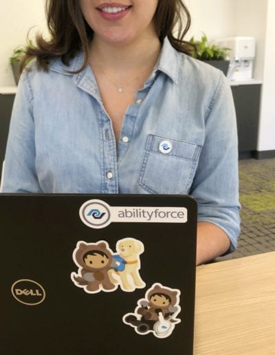 brunette woman working on black laptop with Salesforce and Abilityforce stickers