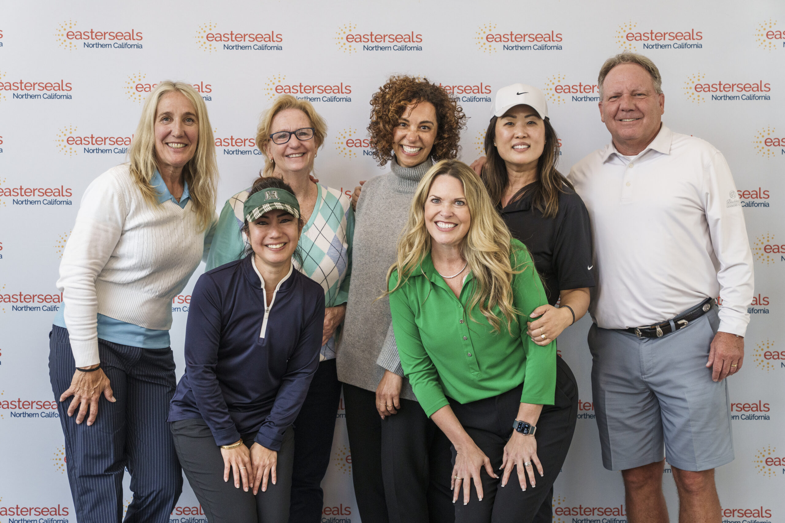 A group of seven smiling colleagues posing together against a step-and-repeat backdrop featuring red logos.
