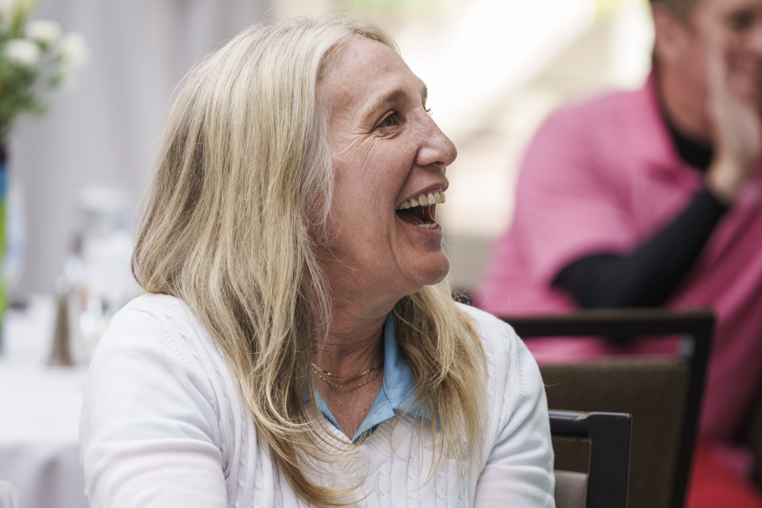 A close-up, candid photo of a blonde woman laughing during a corporate event or presentation.
