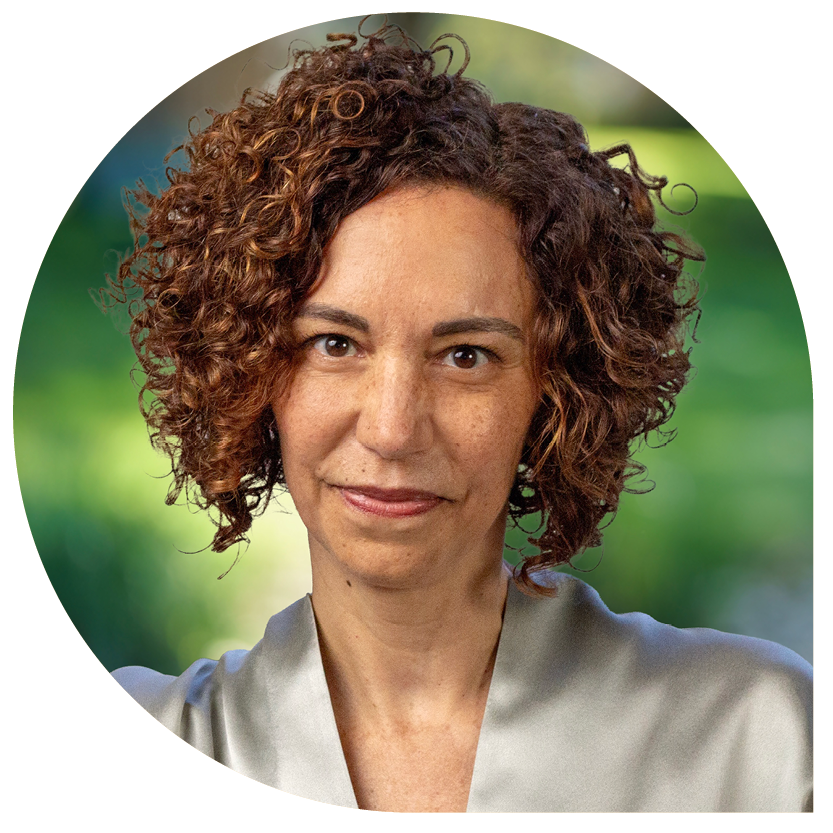 A person with curly brown hair and a soft smile is centered in the image. They wear a gray shirt, with a blurred green background suggesting an outdoor setting.